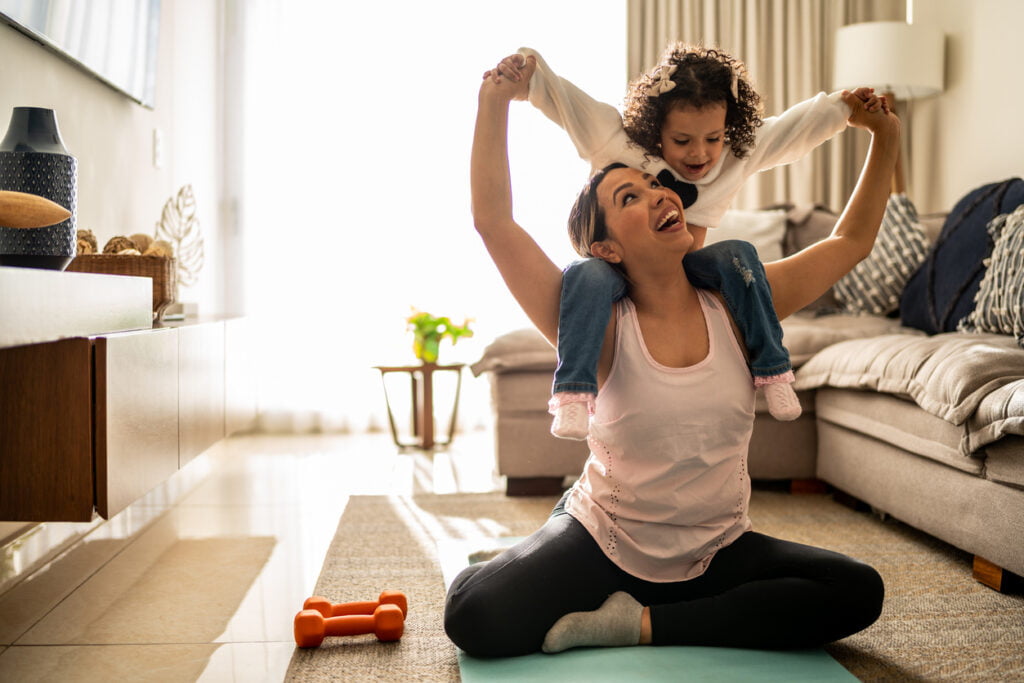 Femme interrompue dans sa séance de gym, jouant avec sa fille dans un salon bien rangé et propre.